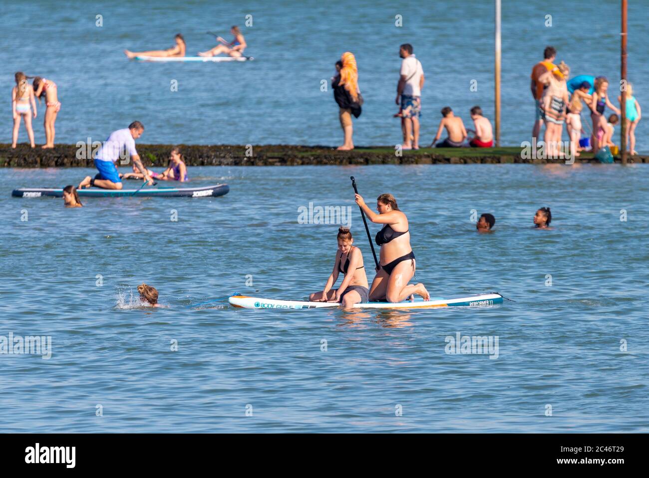 Chalkwell, Southend on Sea, Essex, Royaume-Uni. 24 juin 2020. Avec les températures records de l'année de prévision, les gens se dirigent vers le front de mer pour se rafraîchir, pendant la période d'alerte de séjour du coronavirus COVID-19. À Chalkwell, à l'ouest de Southend on Sea, la rive de l'estuaire de la Tamise est occupée par des paddle-boarders et des nageurs. Deux femelles blanches de race blanche sur une planche Banque D'Images