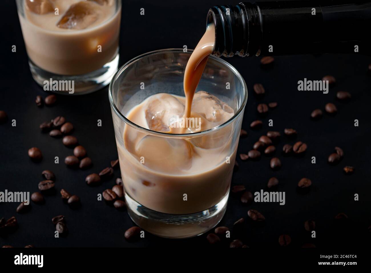 Verser de la crème irlandaise dans un verre de glace, entouré de grains de café sur un fond noir foncé Banque D'Images