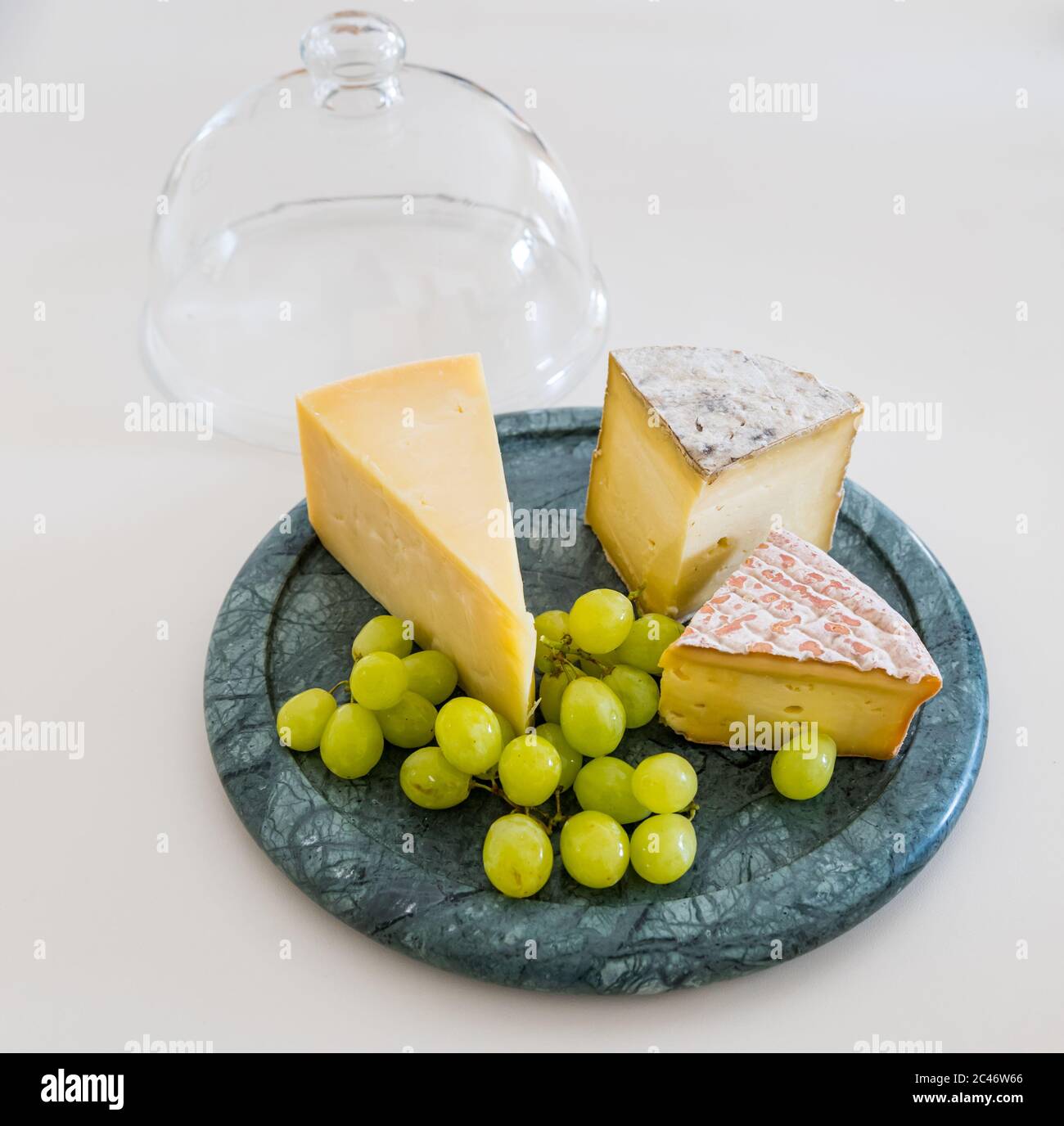 Cheesboard avec cheddar de l'île de Mull, fromage Gorwydd Caerphilly et fromage irlandais Gubbeé avec raisins verts sur comptoir de cuisine blanc Banque D'Images
