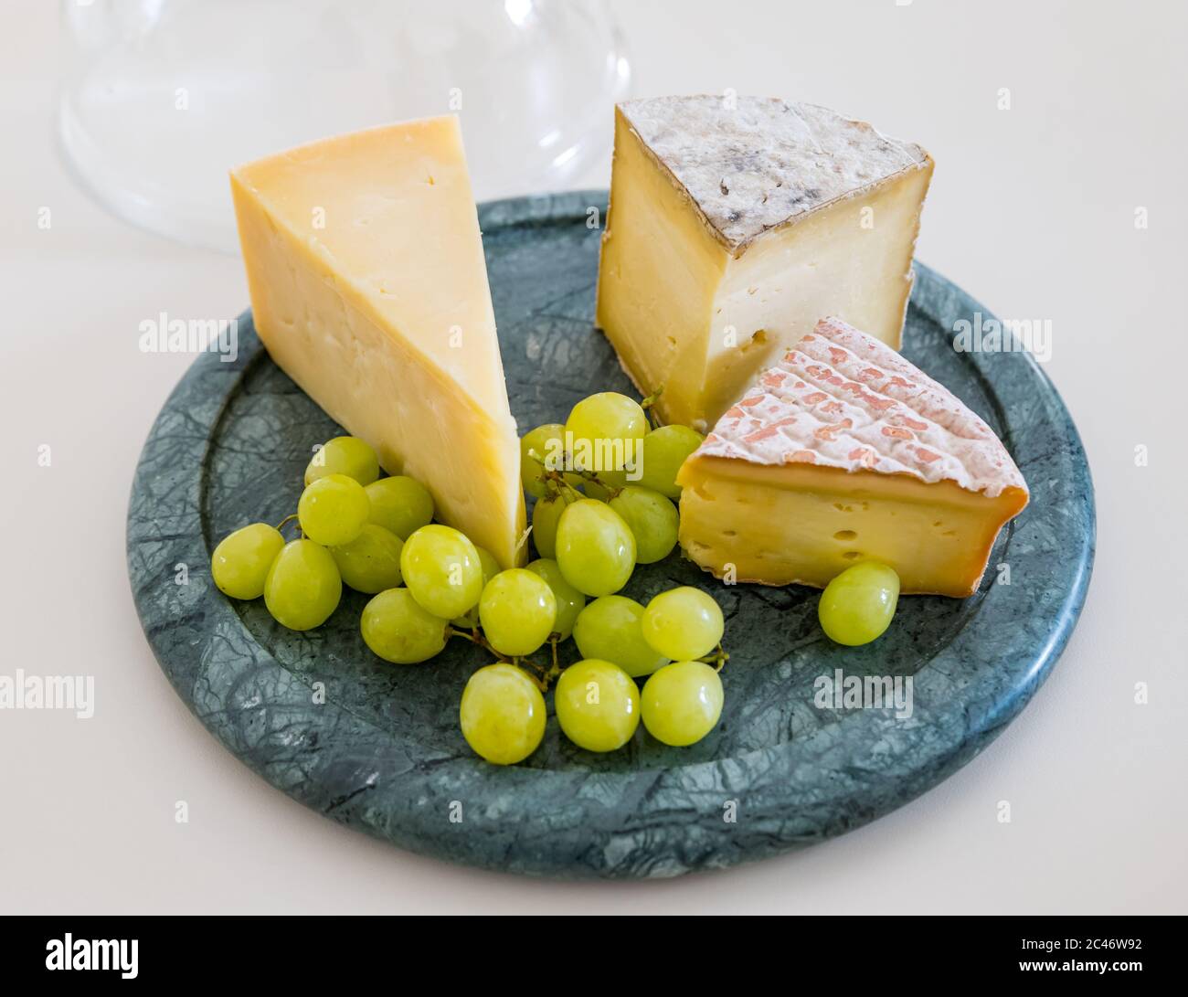 Cheesboard avec cheddar de l'île de Mull, fromage Gorwydd Caerphilly et fromage irlandais Gubbeé avec raisins verts sur comptoir de cuisine blanc Banque D'Images
