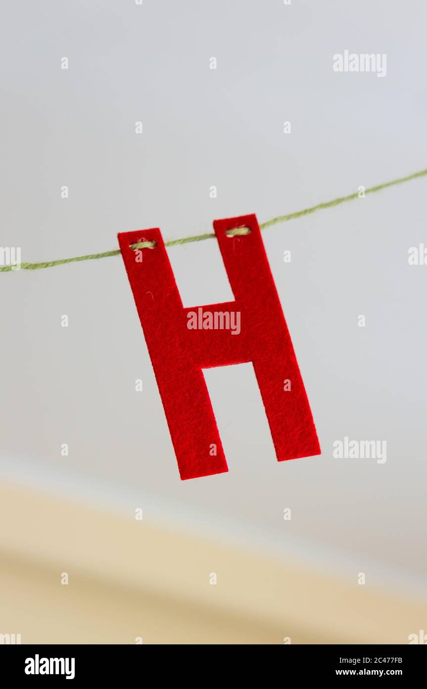 Gros plan d'une lettre H rouge accrochée à un câble avec un arrière-plan flou Banque D'Images
