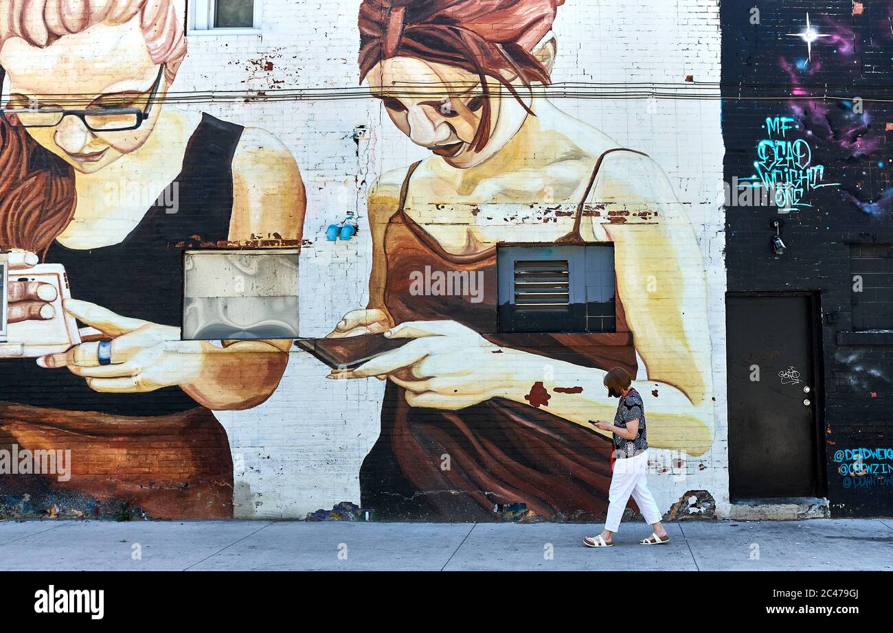 Femme utilisant un téléphone cellulaire devant la murale montrant des femmes utilisant des téléphones cellulaires. La vie imitant l'art l'art imitant la vie. Banque D'Images