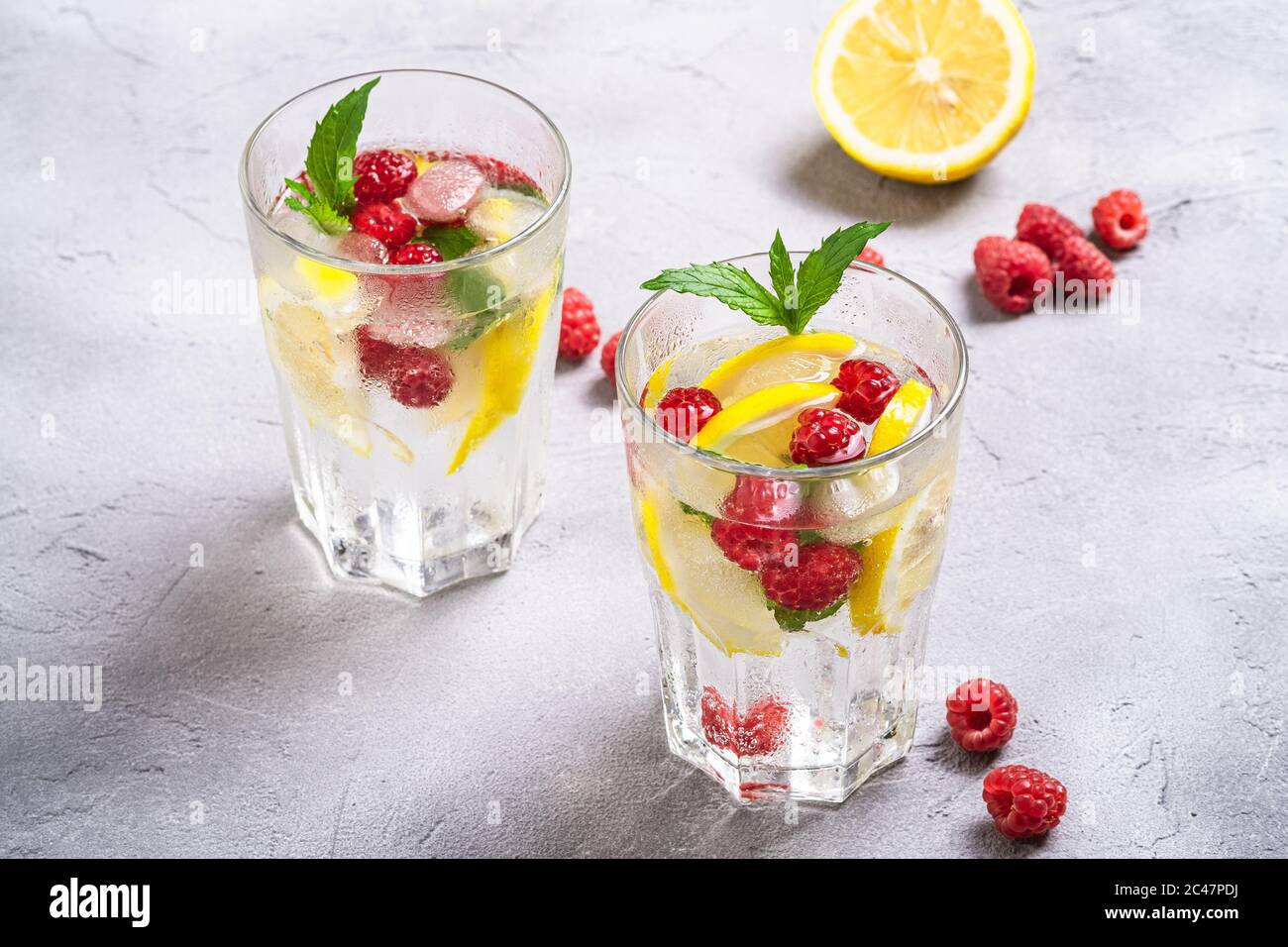 Eau glacée fraîche avec citron, fruits de framboise et feuille de menthe dans deux verre à facettes sur fond de béton de pierre, boisson diététique d'été, vue d'angle Banque D'Images