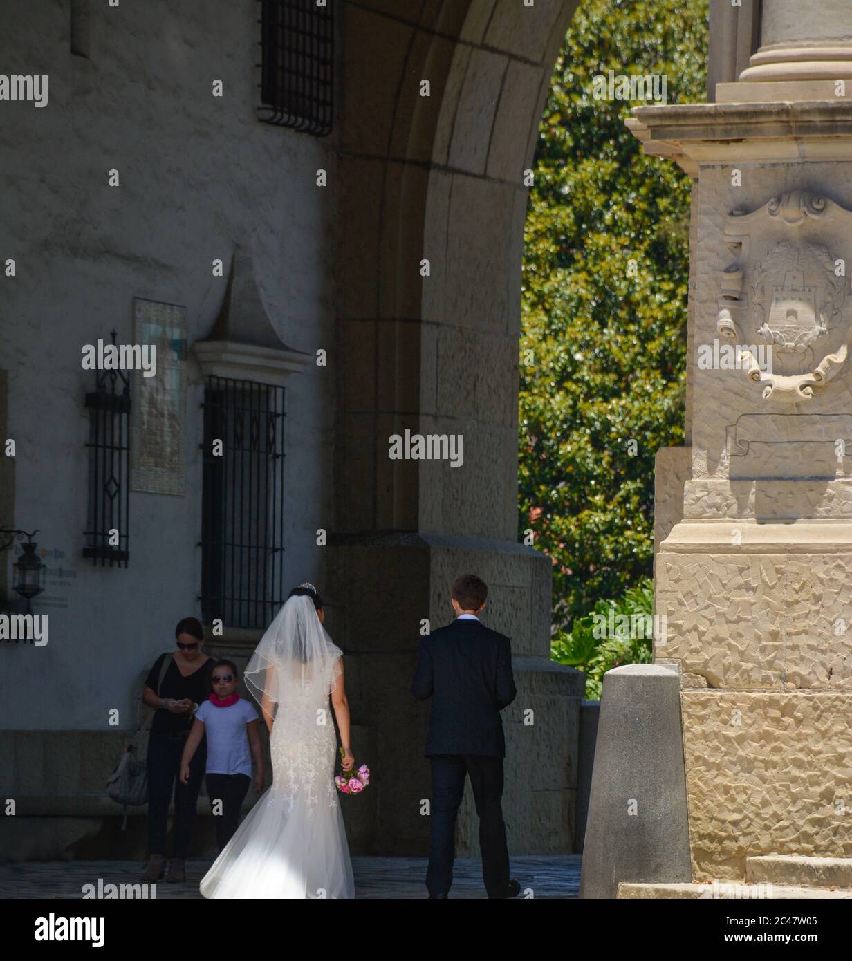 Vue arrière de la mariée et du marié marchant dans l'arcade pillée vers la cour et le jardin en contrebas du palais de justice du comté de Santa Barbara, CA Banque D'Images