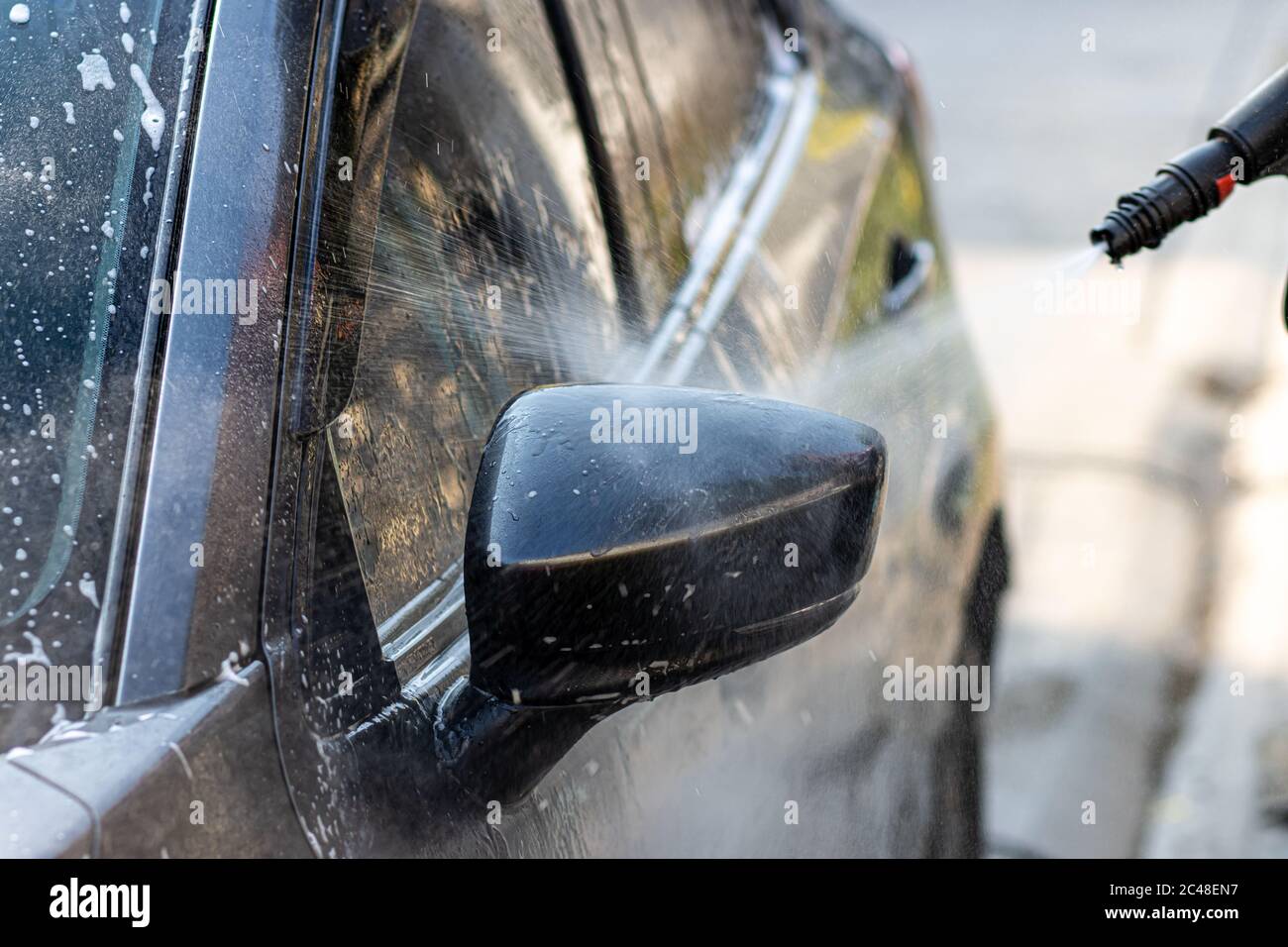 Lavage manuel de la voiture avec eau sous pression à l'extérieur. Homme nettoyant la voiture avec de l'eau sous haute pression dans une rue. Banque D'Images