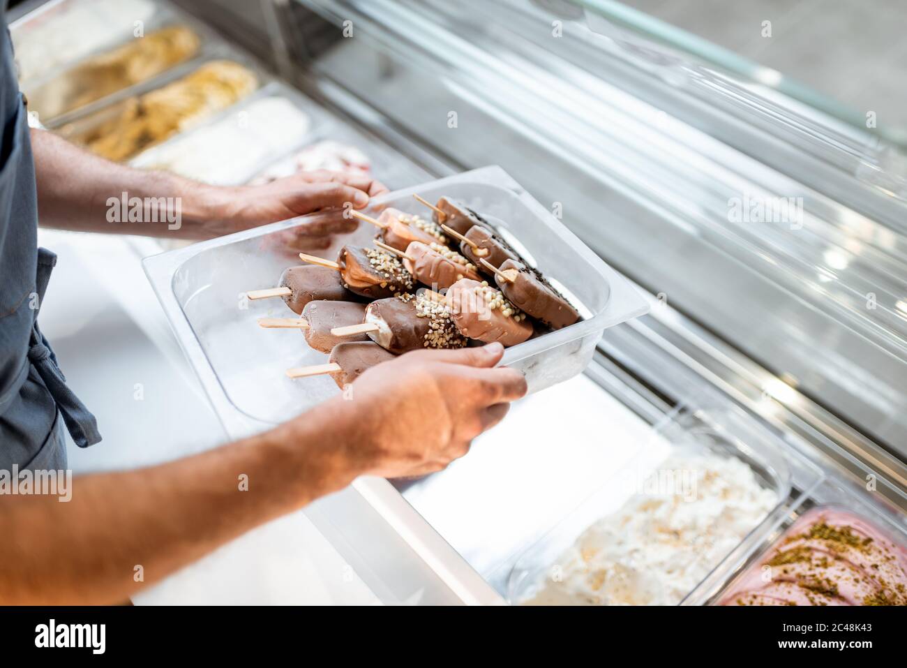 Vendeur mettant plateau avec glace sur un bâton dans le frigo au comptoir d'un magasin, gros plan Banque D'Images