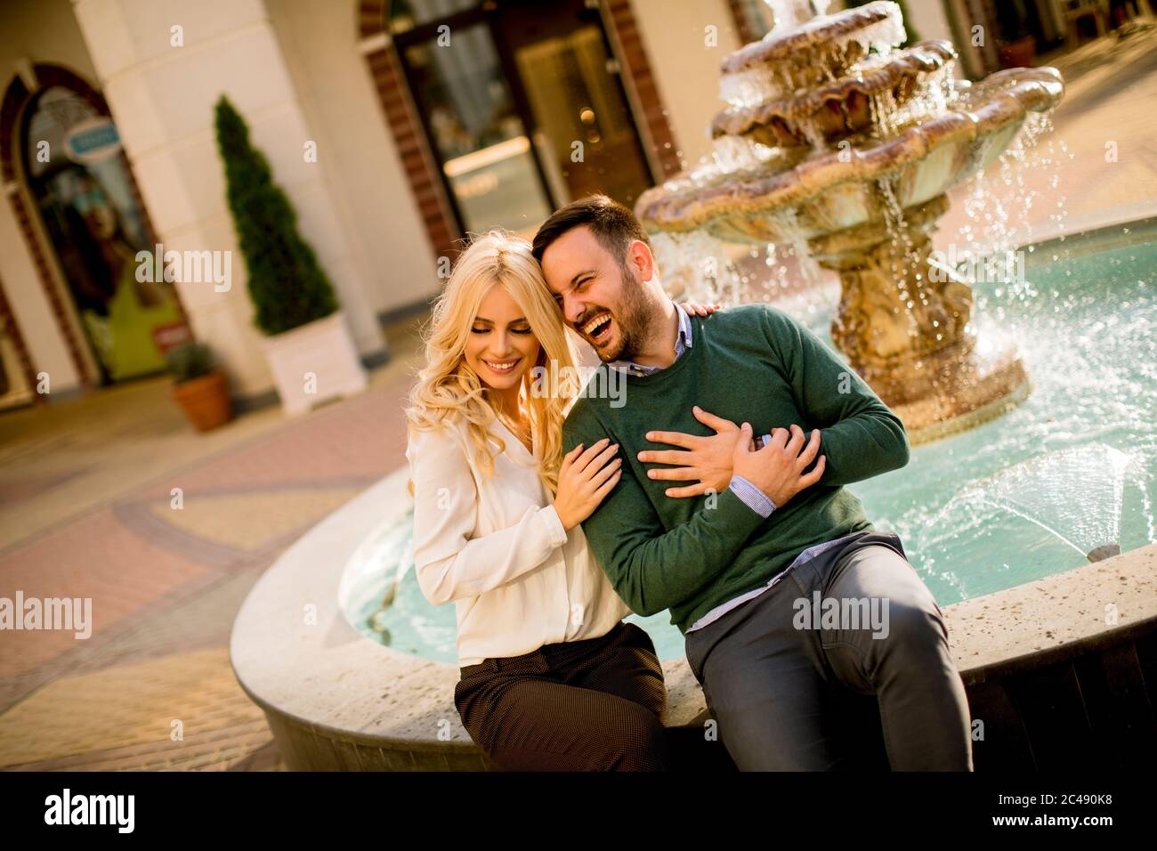 Portrait d'un beau couple d'amour souriant assis près d'une fontaine par un beau jour Banque D'Images
