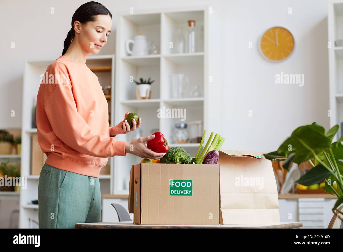 Jeune femme recevant la livraison de nourriture à la maison elle prend les légumes hors de la boîte Banque D'Images