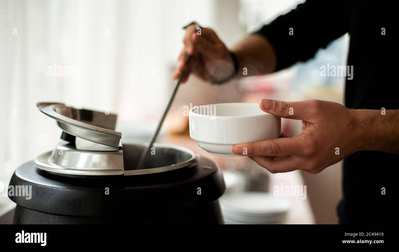 Une main de homme tient une louche et met sur la soupe, UN homme versant la soupe dans le plat blanc de la reen Banque D'Images