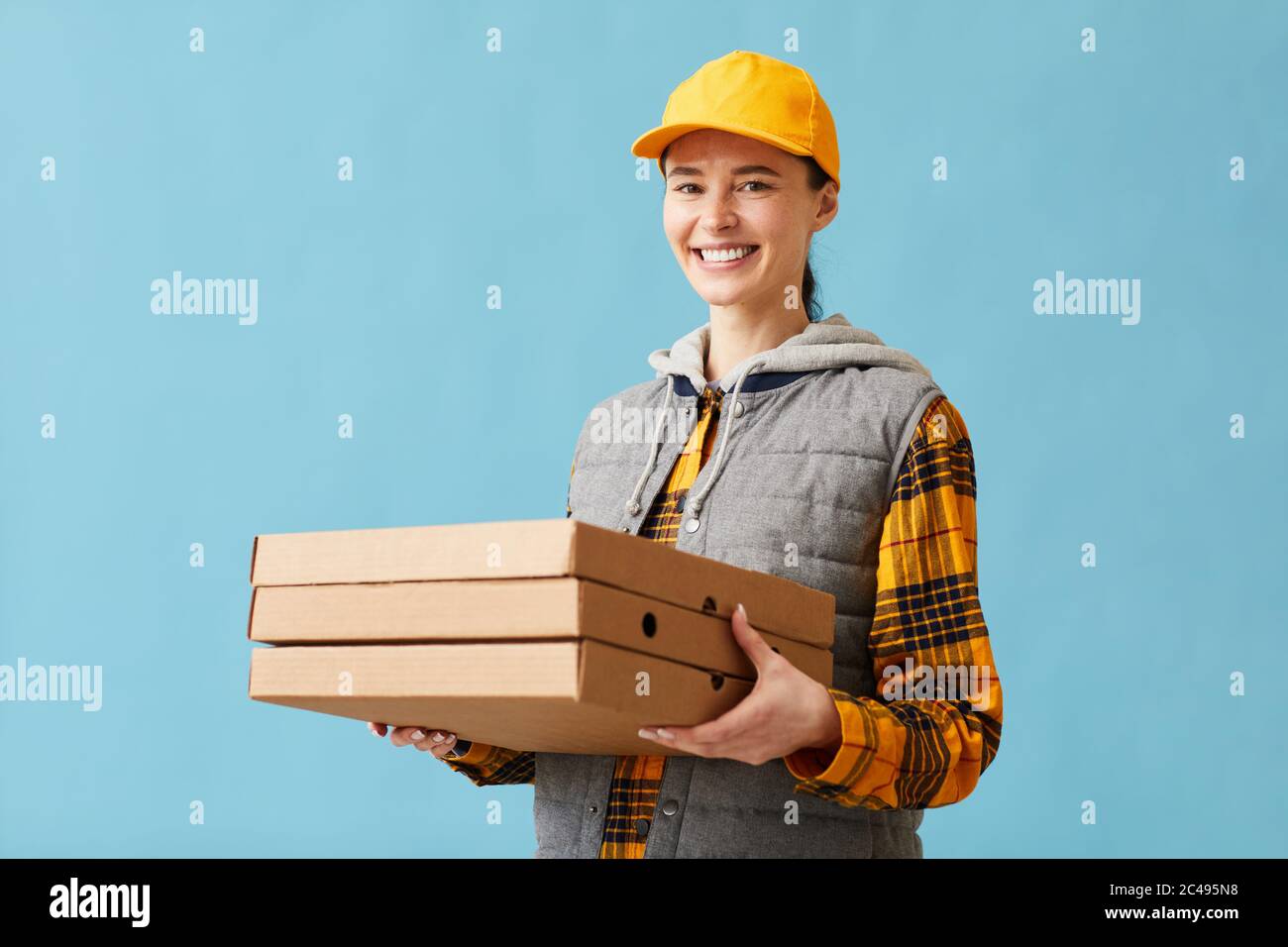 Portrait de la jeune femme en uniforme souriant à la caméra et livrant la pizza qu'elle se tient sur le fond bleu Banque D'Images