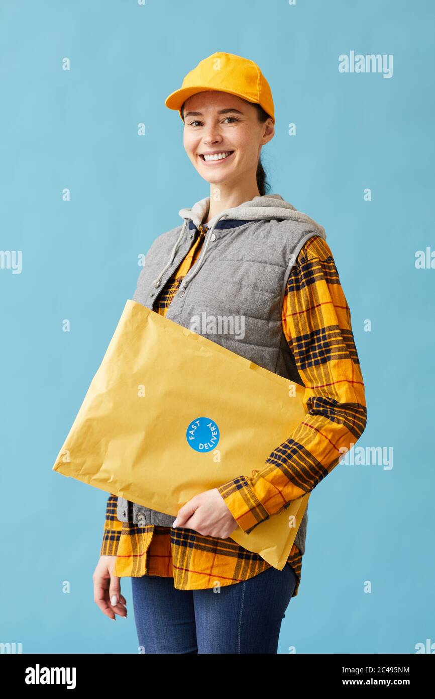 Portrait de jeune postataire en uniforme tenant une grande parcelle et souriant à la caméra isolée sur fond bleu Banque D'Images