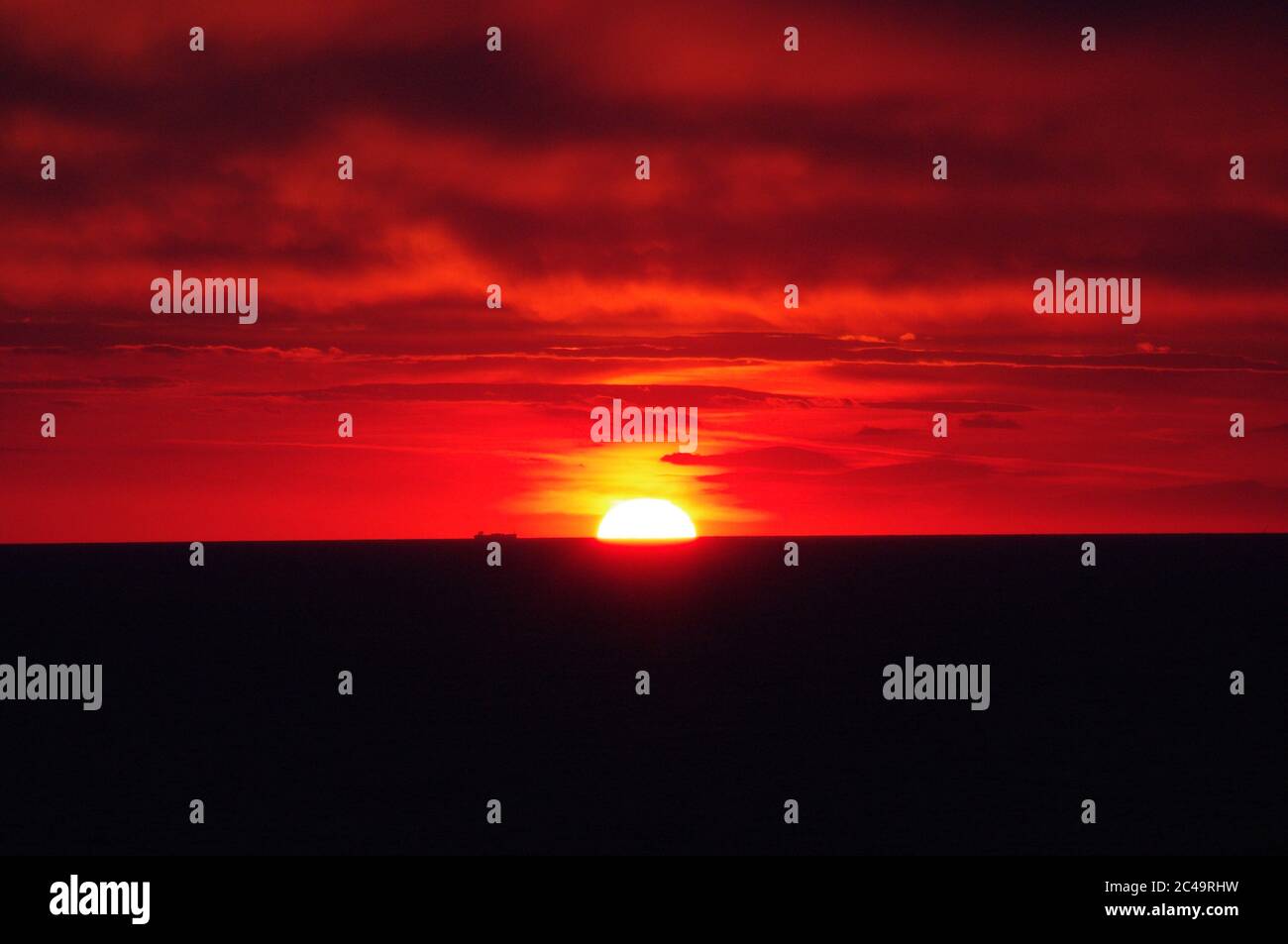 Séquence d'images d'un coucher de soleil, coucher de soleil rouge vif sur mer sombre avec nuages sombres Banque D'Images