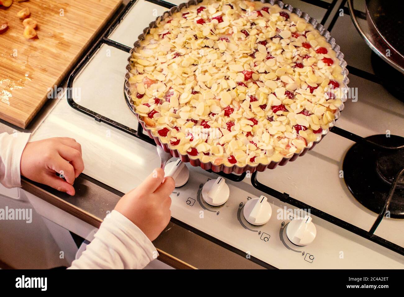 le jeune garçon cuit et cuit la tarte aux cerises avec des tranches d'amande avec son mamme Banque D'Images