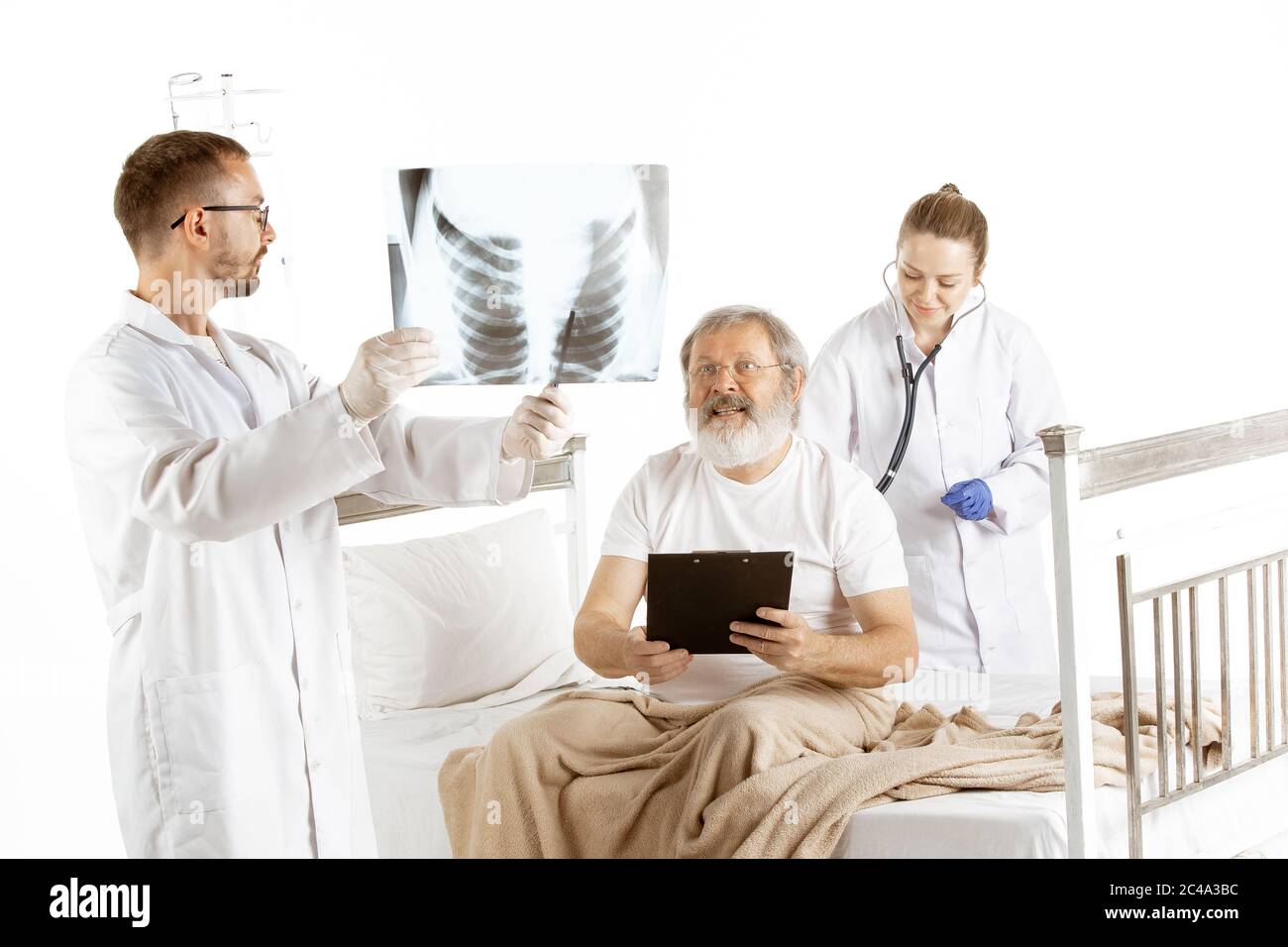 Vieux homme âgé se rétablissant dans un lit d'hôpital isolé sur fond blanc. Concept de santé et de médecine, diagnostic. Infirmière écouter l'inspiration avec le stéthoscope pendant que le médecin montre l'examen pulmonaire. Banque D'Images