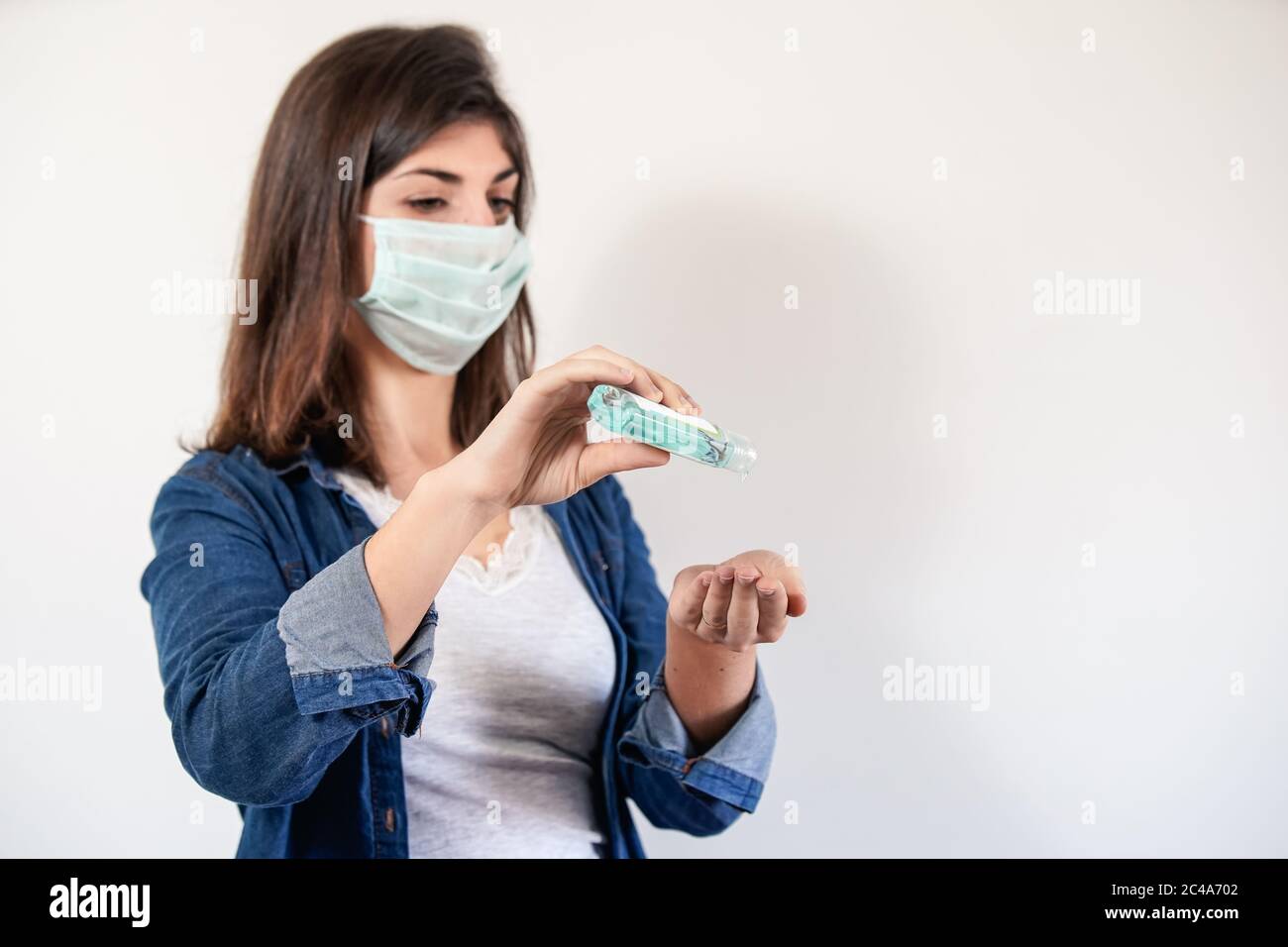 Femme avec masque de protection médicale mettant sur antiseptique pour désinfecter ses mains Banque D'Images