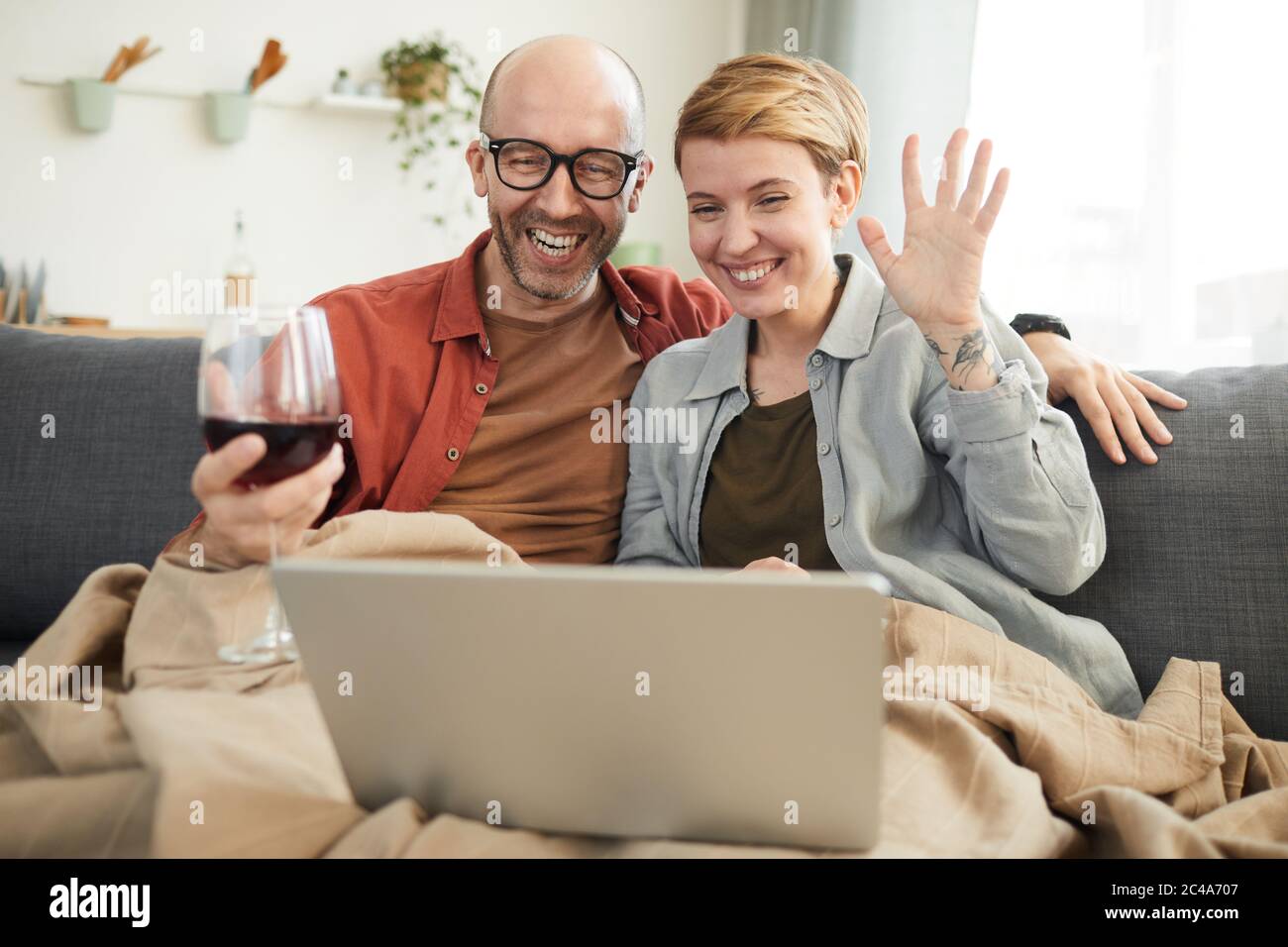 Jeune couple heureux de boire du vin rouge et de communiquer en ligne avec leurs amis à la maison Banque D'Images