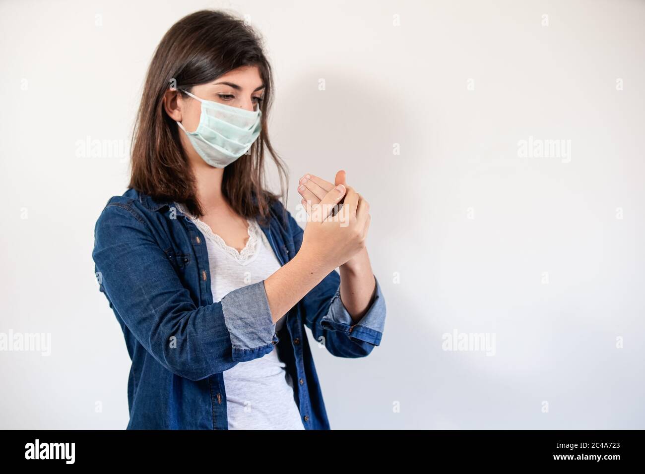 Femme avec masque de protection médicale mettant sur antiseptique pour désinfecter ses mains Banque D'Images
