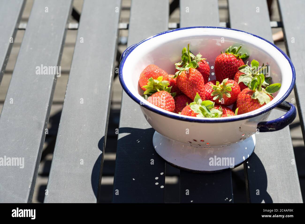 Bol de fraises fraîches dans un bol blanc ou passoire sur une table en bois noir à l'extérieur Banque D'Images