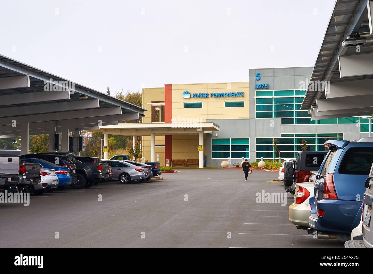 Une femme marche dans un parking plein de voitures à Kaiser permanente à Santa Rosa, Californie. Le toit de panneau solaire couvre le terrain. Banque D'Images