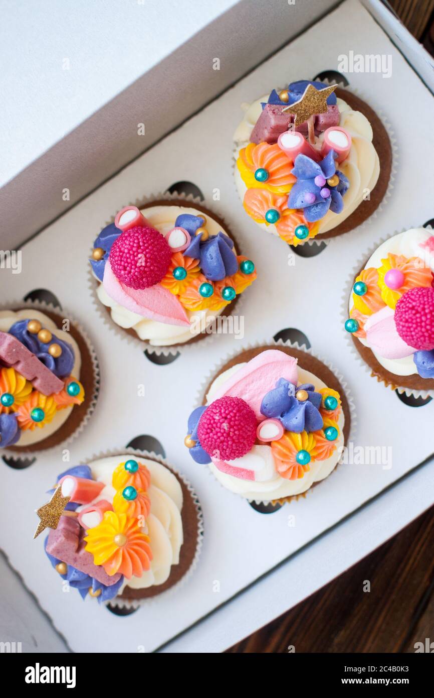 Petits gâteaux au chocolat de fête avec décoration au fromage blanc rose, étoiles dorées, bonbons et guimauves dans une boîte cadeau. Banque D'Images