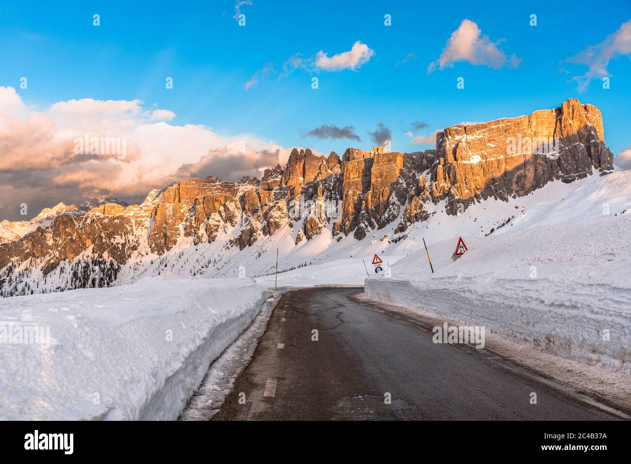 Une route vide et droite du col de montagne dans un magnifique paysage enneigé avec des sommets rocheux imposants et chaleureusement éclairés par un soleil couchant en hiver Banque D'Images