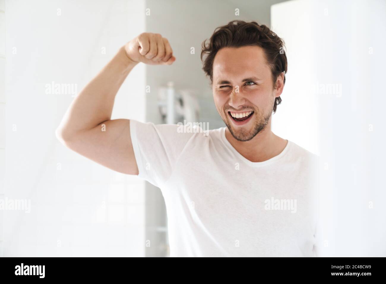 Attrayant heureux confiant jeune homme debout devant le miroir de salle de bains, flexion biceps Banque D'Images