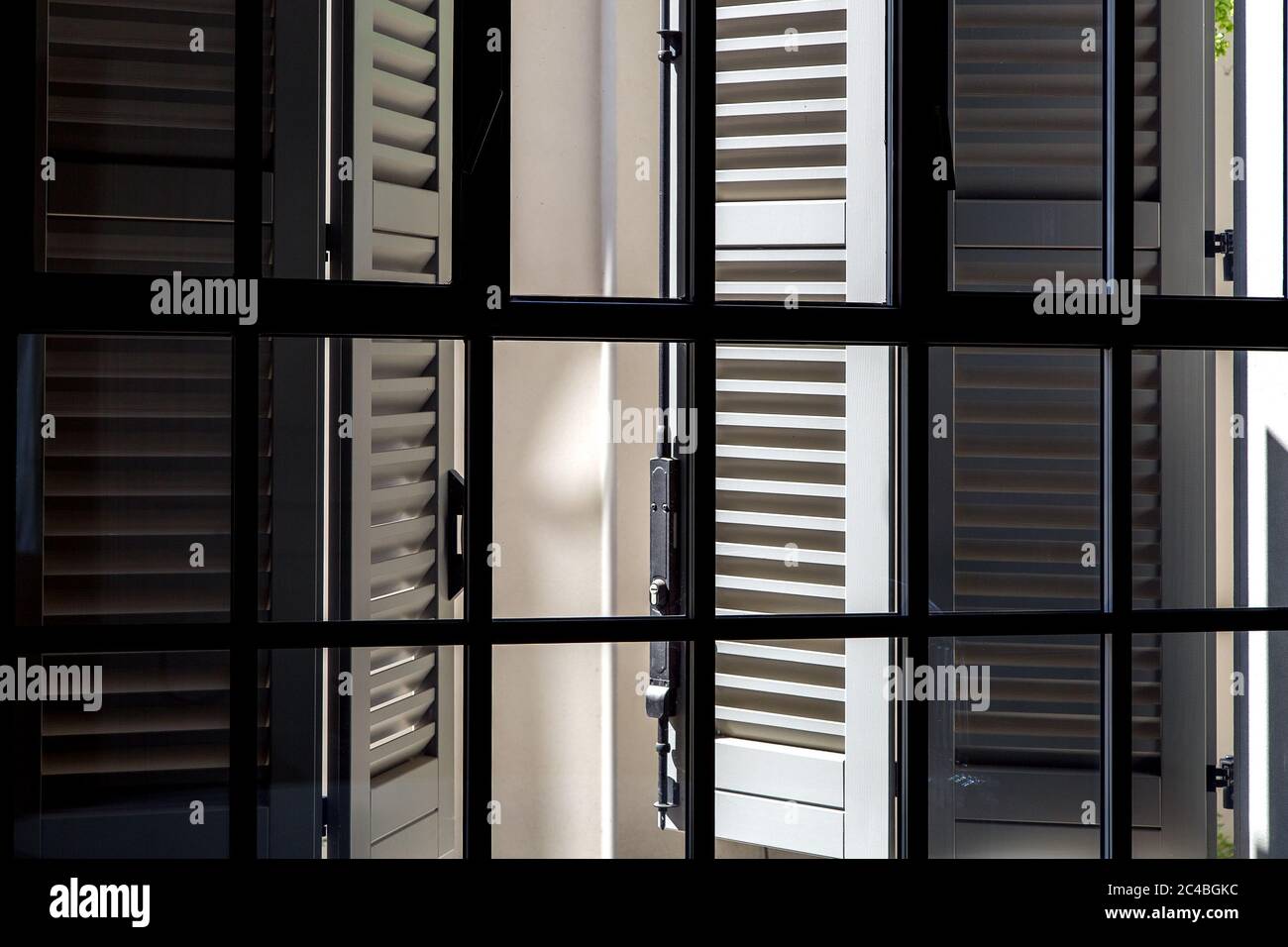 Volets en bois gris sur une vue de jour ensoleillée de l'intérieur par une fenêtre avec un cadre noir et verre, volets italiens traditionnels sur une journée ensoleillée. Banque D'Images