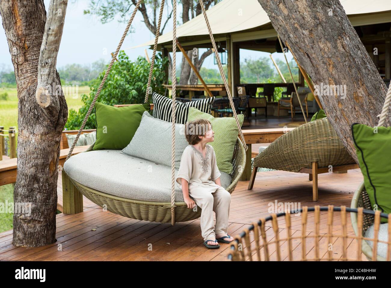 Garçon de 6 ans assis sur une balançoire, camp de tented, Botswana Banque D'Images