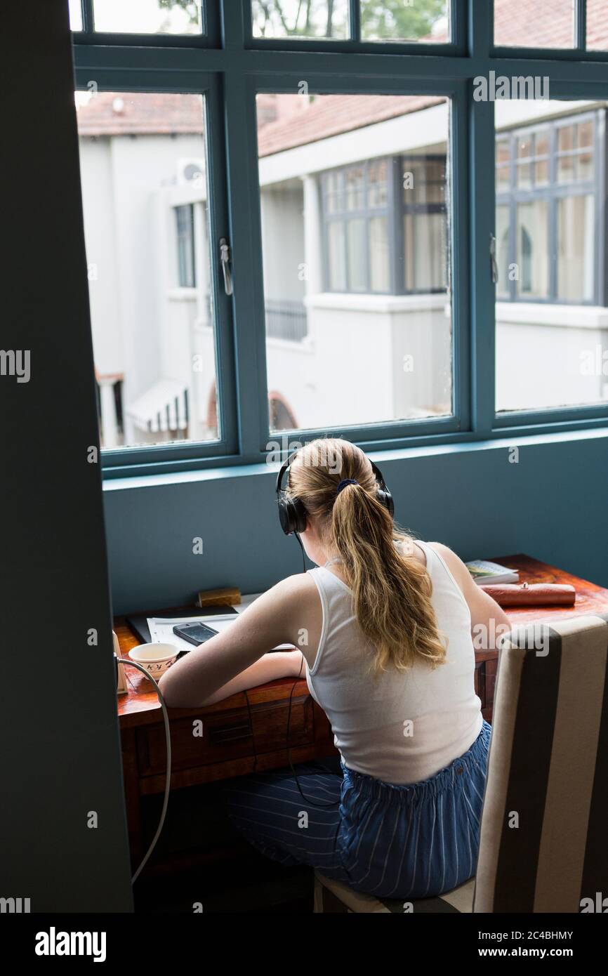 Une fille de treize ans portant un casque faisant ses devoirs assis dans un endroit calme. Banque D'Images