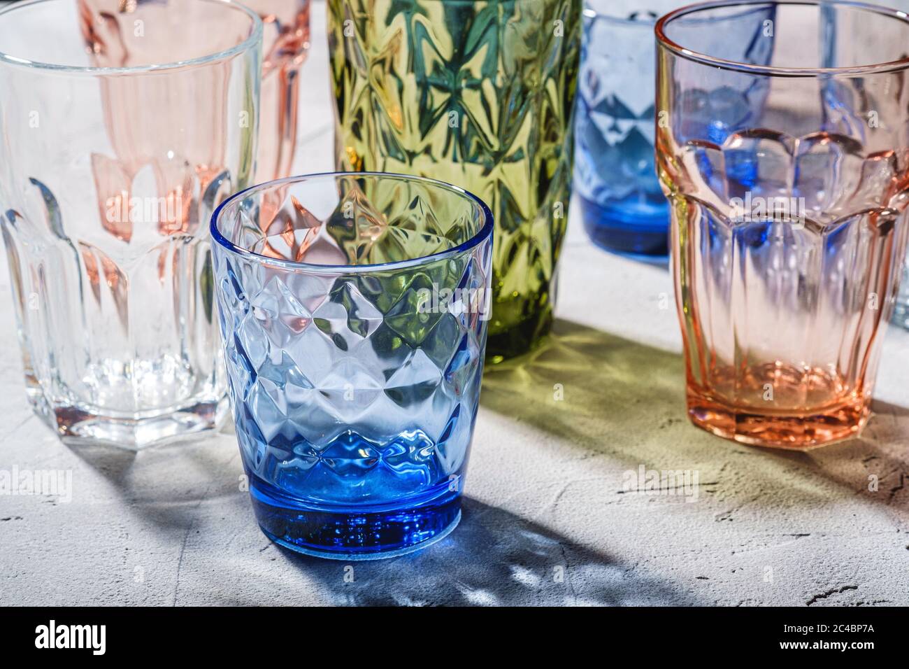Verre à boire coloré à facettes et géométrique, ensemble de verres vides  verts, rouges, bleus et transparents pour boissons sur fond de béton de  pierre, angle Photo Stock - Alamy
