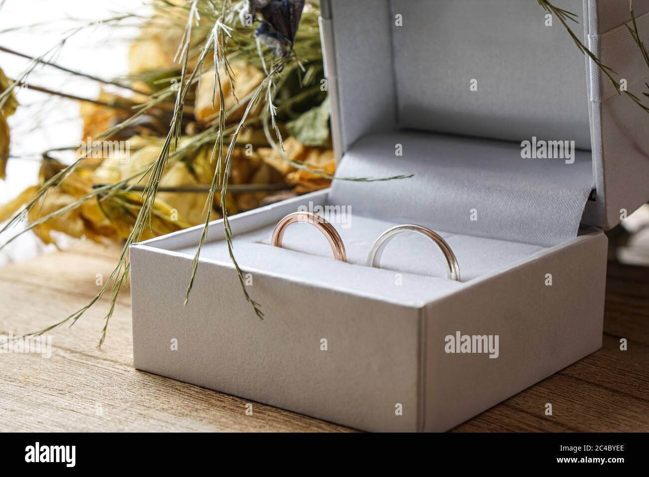 Anneaux d'engagement or et argent à l'intérieur de la boîte en velours blanc . Concept de proposition. Fleurs de mariage en arrière-plan. Banque D'Images