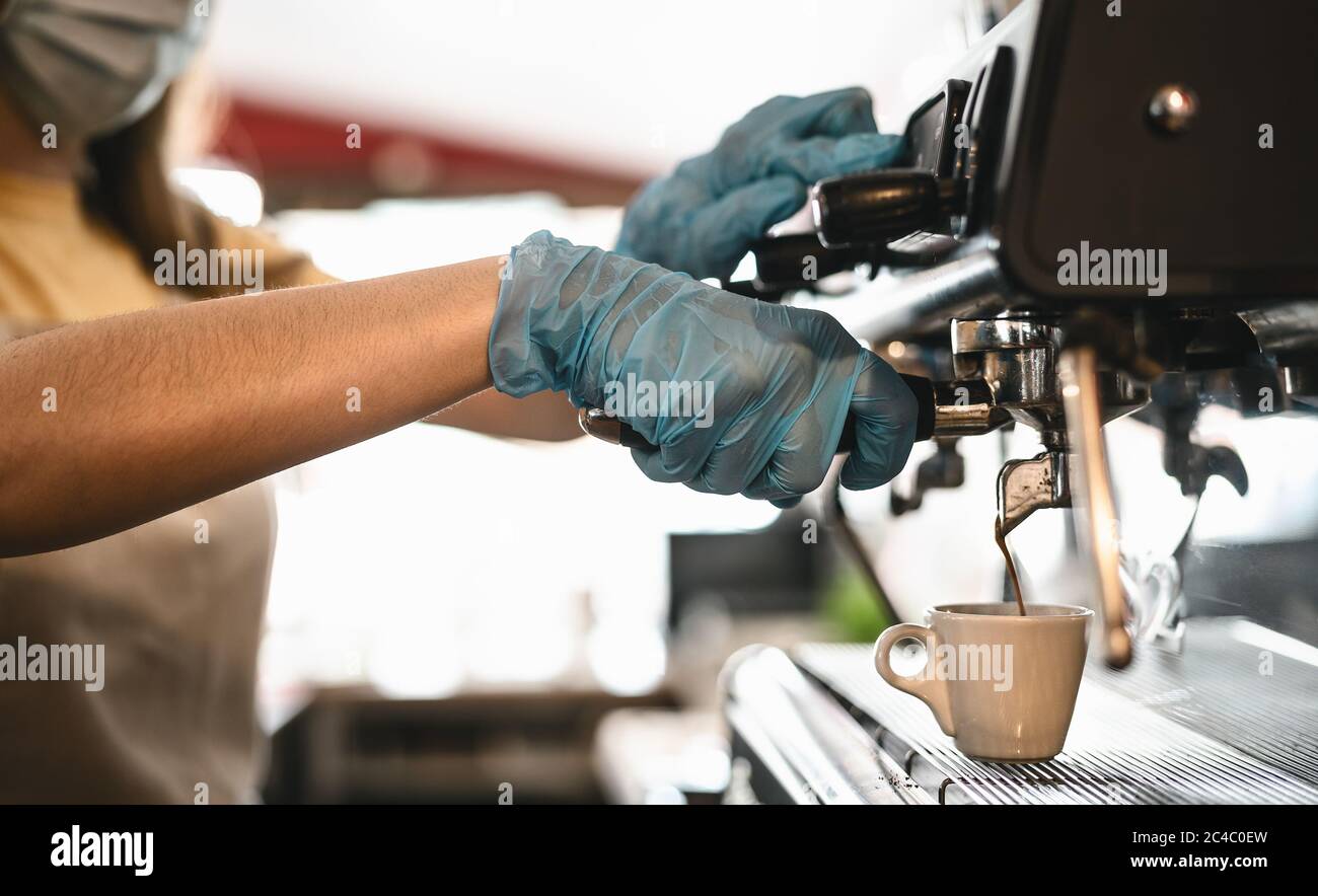 Jeune femme vue latérale faire un café expresso tout en portant un masque chirurgical et des gants pour prévenir la propagation du virus corona - le propriétaire du bar sécurité de travail Banque D'Images