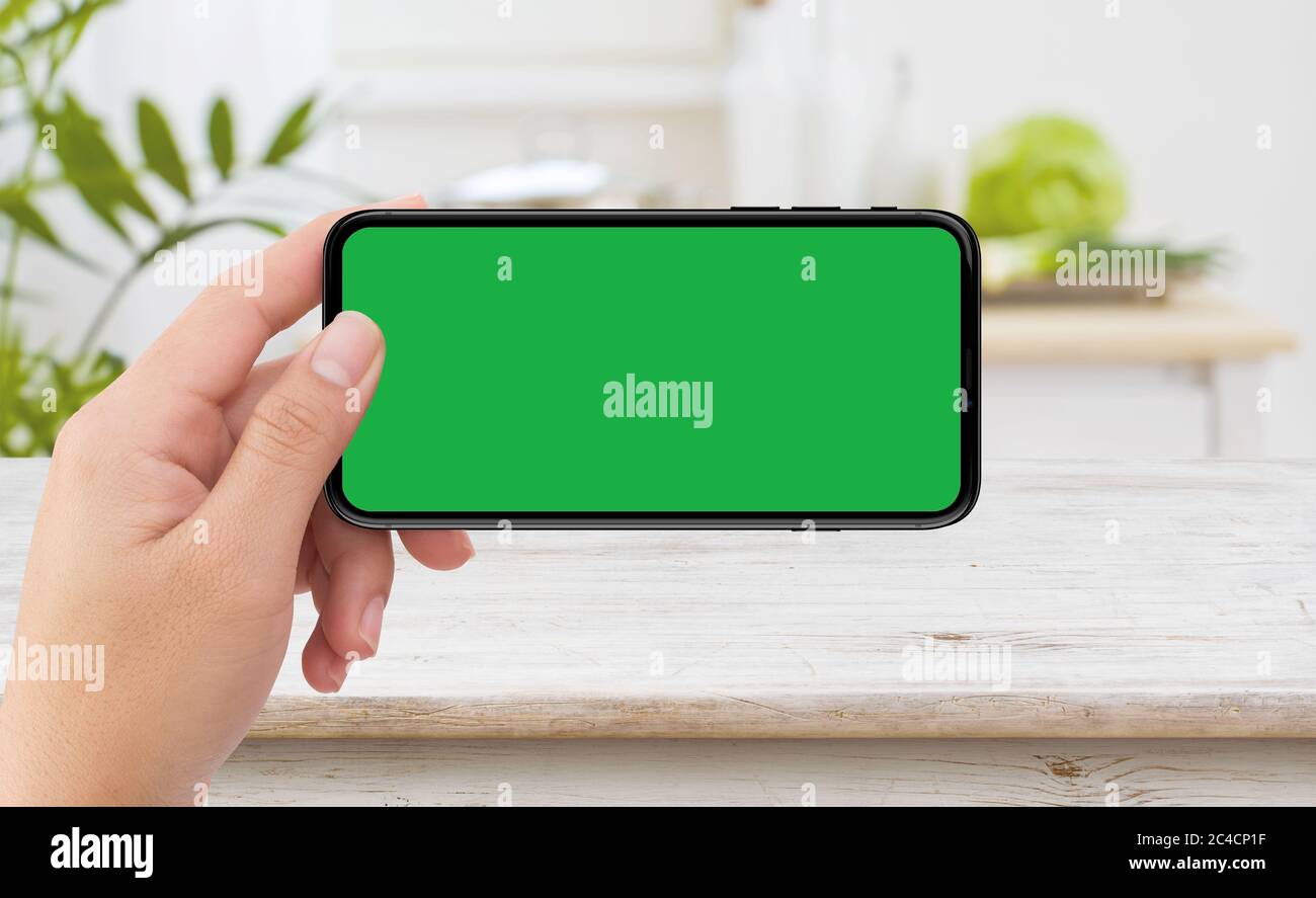 Main gauche isolée tenant un smartphone mobile noir avec écran vert au kichen intérieur Banque D'Images