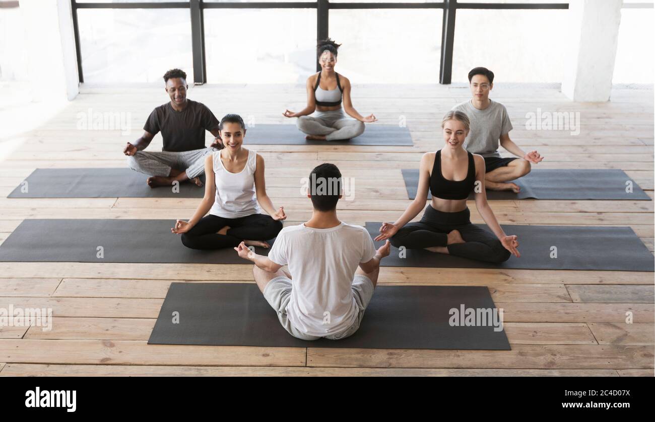 Groupe de jeunes ayant cours de yoga avec entraîneur en studio Banque D'Images
