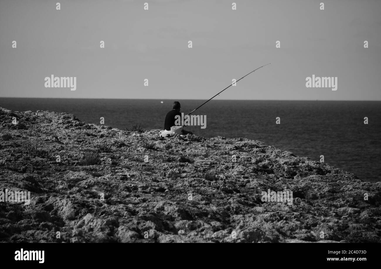 MELLIEHA, MALTE - 12 octobre 2014 : un homme pêchant seul en paix sur une falaise à Malte, regardant vers l'horizon, assis sur le paysage karstique calcaire ro Banque D'Images