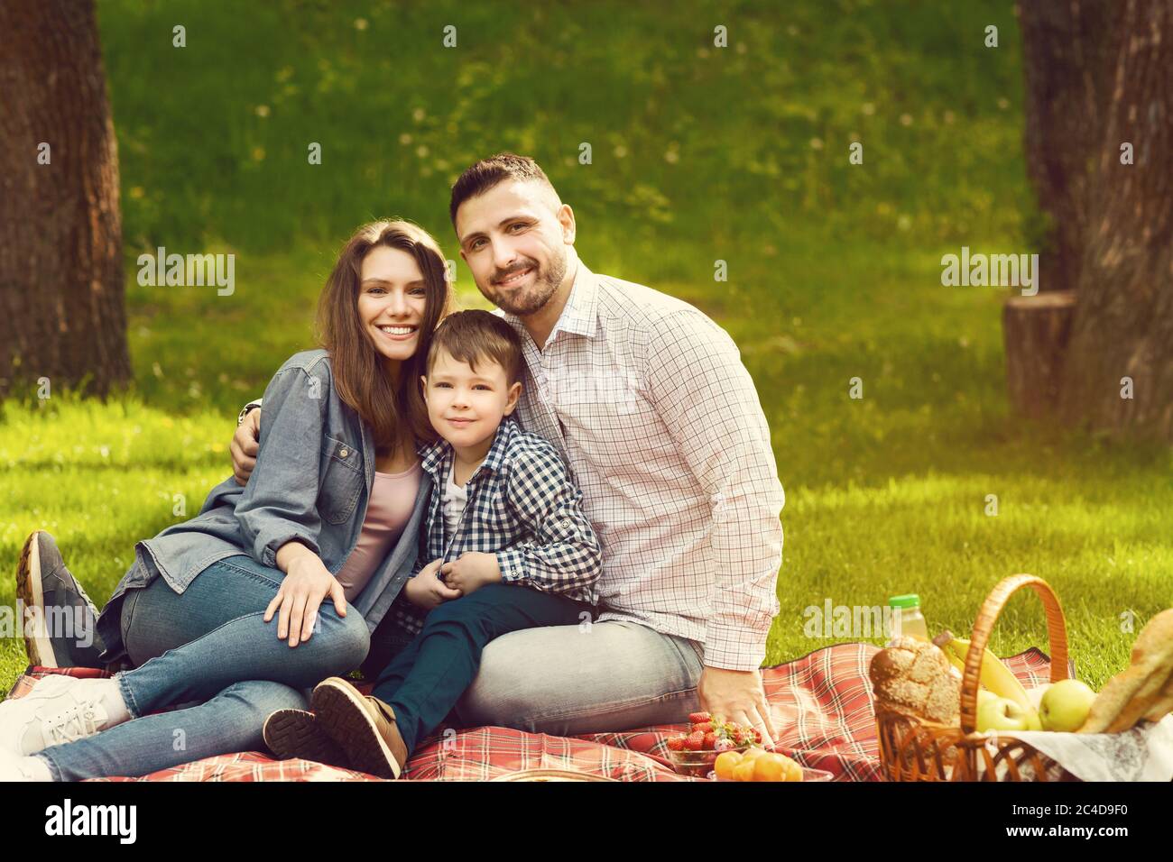 Famille heureuse avec un enfant mignon en train de profiter de son temps sur pique-nique dans le parc, espace vierge Banque D'Images