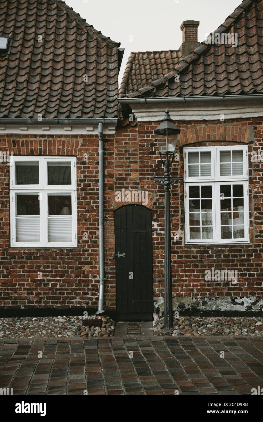 Étroite porte en bois entre les vieilles maisons en briques avec fenêtres encadrées blanches avec la lampe de rue et la route en pierre en face d'eux Banque D'Images