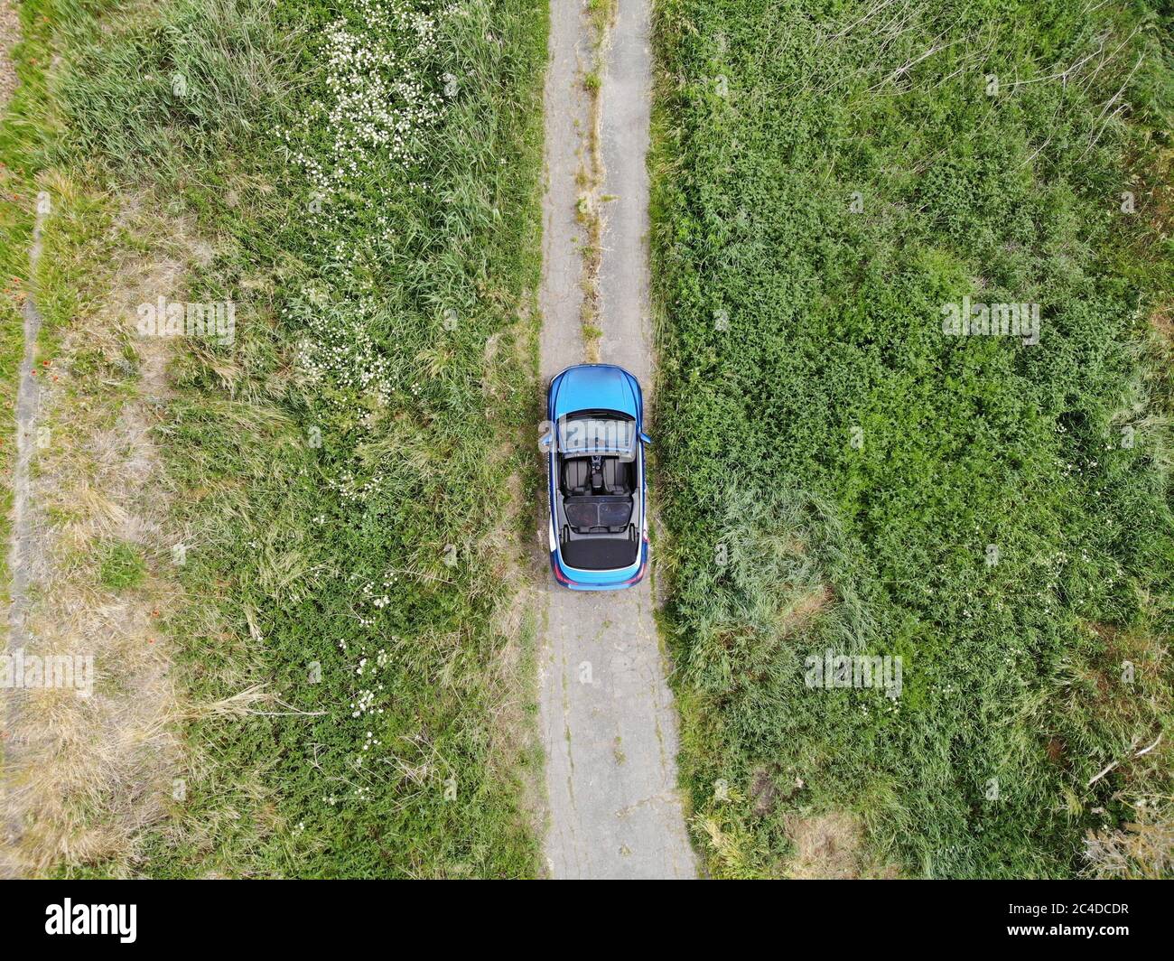 Photo aérienne du cabriolet bleu vide cabrio sur route de terre au champ vert Banque D'Images