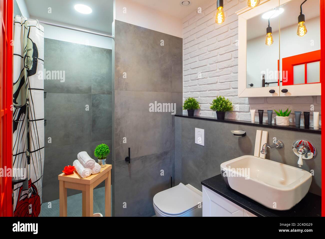 Intérieur loft moderne de la salle de bains. Lavabo et toilettes blancs. Mur de briques. Carreaux gris. Porte rouge. Banque D'Images