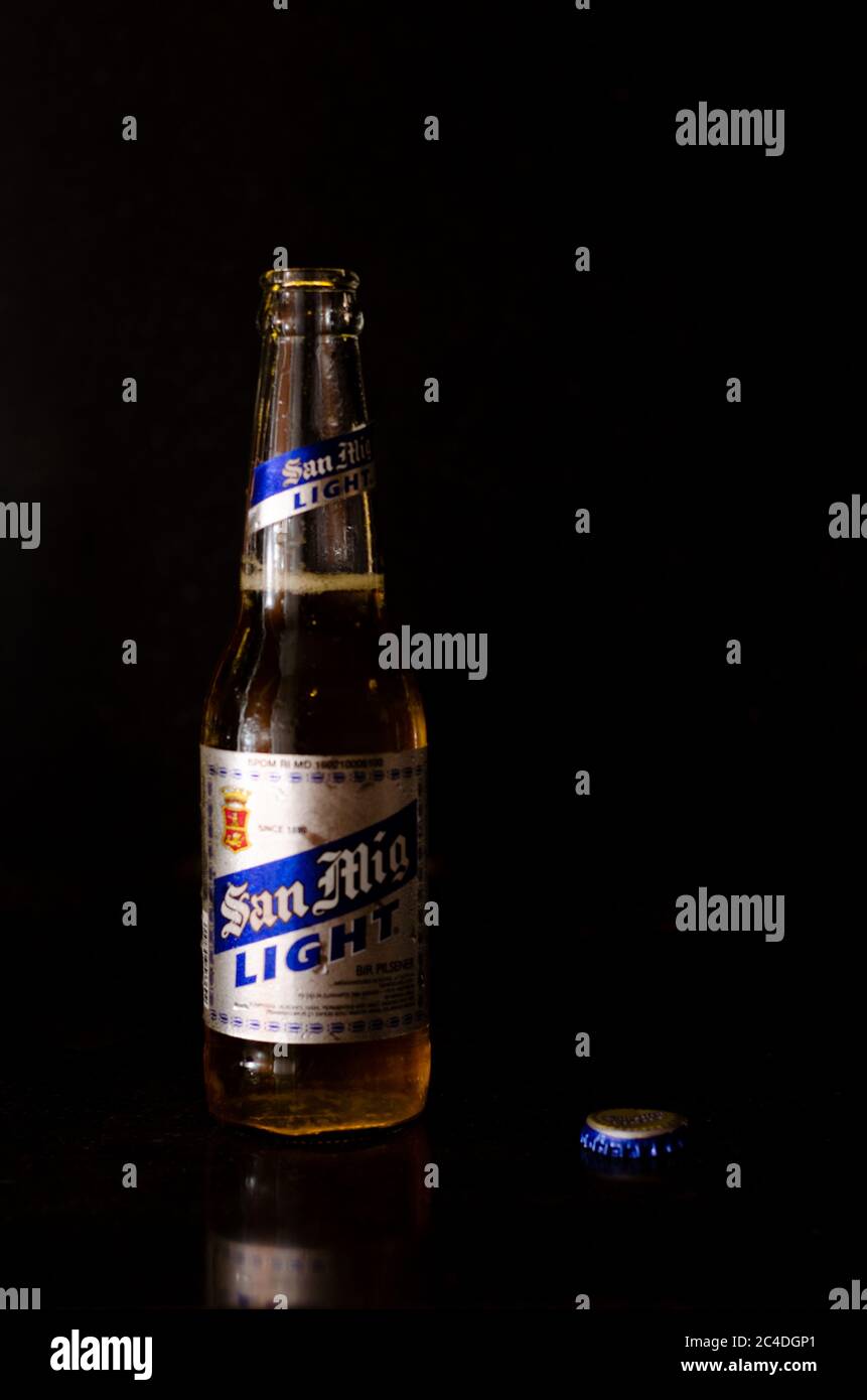 Vue de face de la bière légère San Miguel avec étiquette argentée et bleue, le couvercle à côté dans un fond en marbre noir Banque D'Images