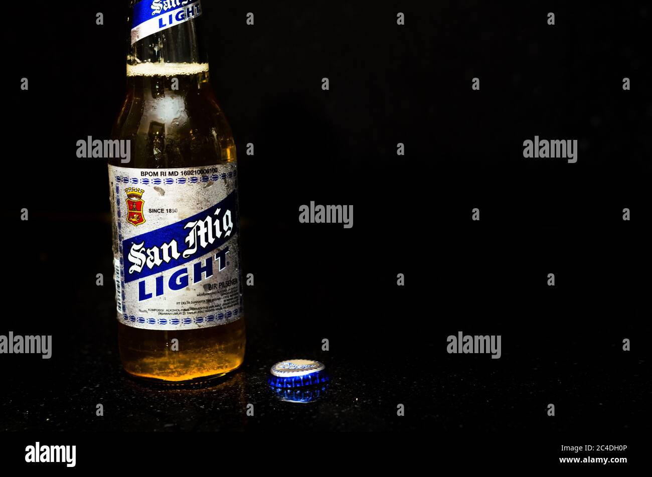 Vue de face de la bière légère San Miguel avec étiquette argentée et bleue, le couvercle à côté dans un fond en marbre noir Banque D'Images