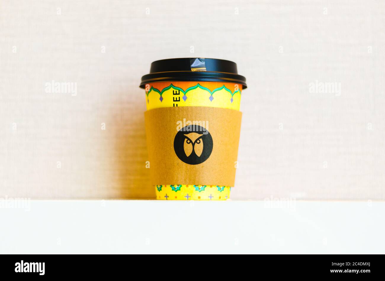 Une tasse de café jaune à emporter avec le logo Maxx Coffee Chain Owl au centre du papier isolant thermique. Banque D'Images