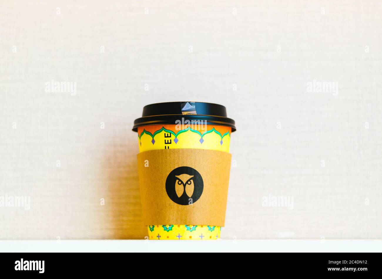 Une tasse de café jaune à emporter avec le logo Maxx Coffee Chain Owl au centre du papier isolant thermique. Banque D'Images