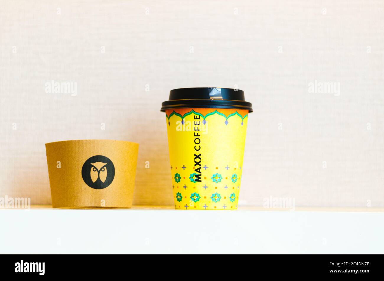 Une tasse de café jaune à emporter avec le logo Maxx Coffee Chain Owl au centre du papier isolant thermique. Banque D'Images
