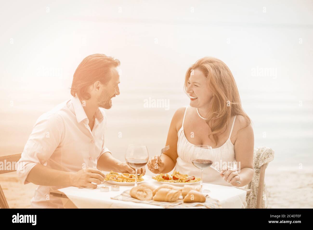 Les romantiques passent du temps ensemble sur fond de mer. Un couple de Caucasiens heureux se reposant dans un café de plage le jour d'été ensoleillé. Image teintée Banque D'Images