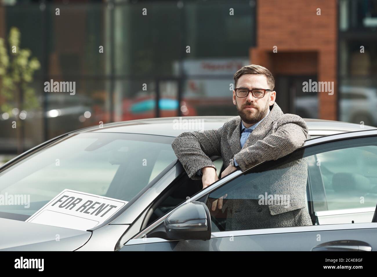 Portrait d'un homme d'affaires à barbe mûr en lunettes regardant l'appareil photo tout en se tenant près de la voiture à l'extérieur Banque D'Images