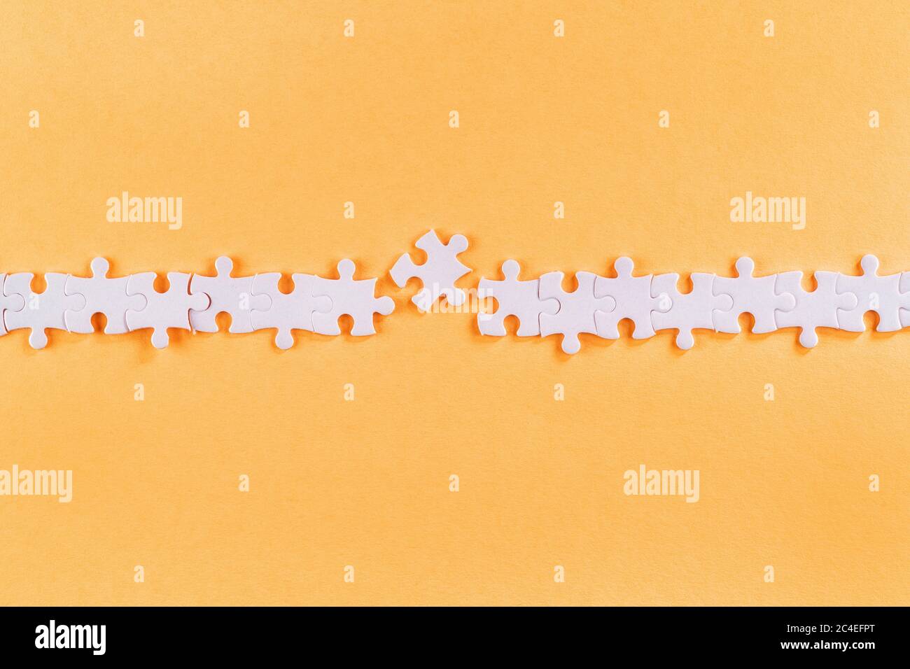 Rangée de pièces de puzzle blanches perturbées avec lien manquant sur fond orange Banque D'Images
