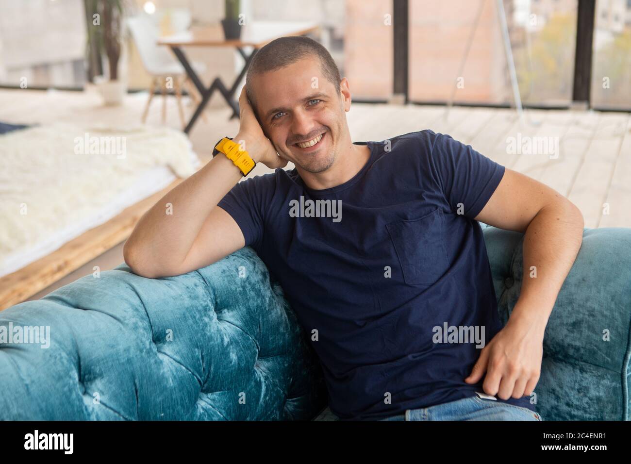 Homme souriant regardant dans l'appareil photo assis sur le canapé Banque D'Images