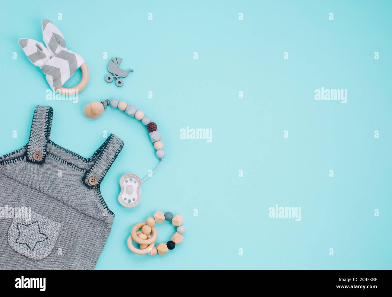 Concept d'accessoires pour bébé. Barboteuse, sucette et jouets en bois pour bébé sur fond bleu avec espace vide pour le texte. Vue de dessus, plan d'appartement. Banque D'Images