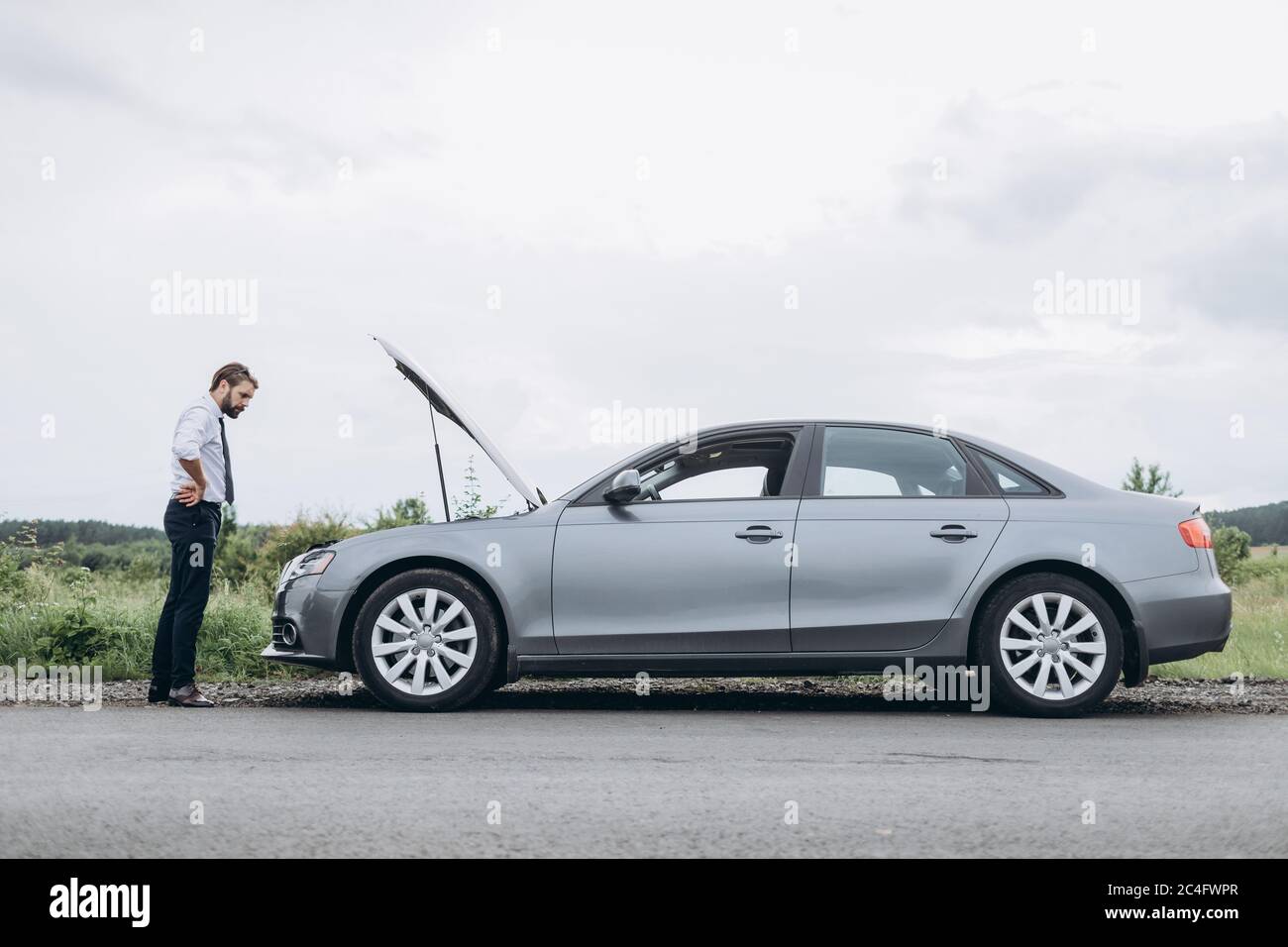 Homme stressé à la recherche d'une cause de défaillance sous le capot de la voiture Banque D'Images